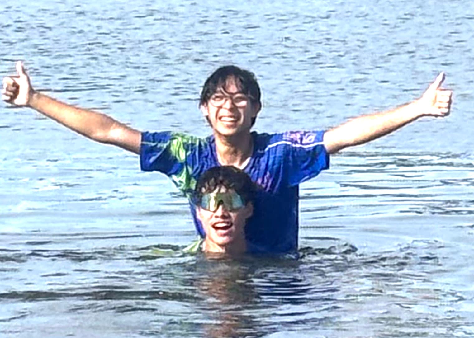 Torix co-founders Steven Sah and Ian Wang standing in open water, one behind with arms spread and thumbs up, one in front up to the chin in sport sunglasses